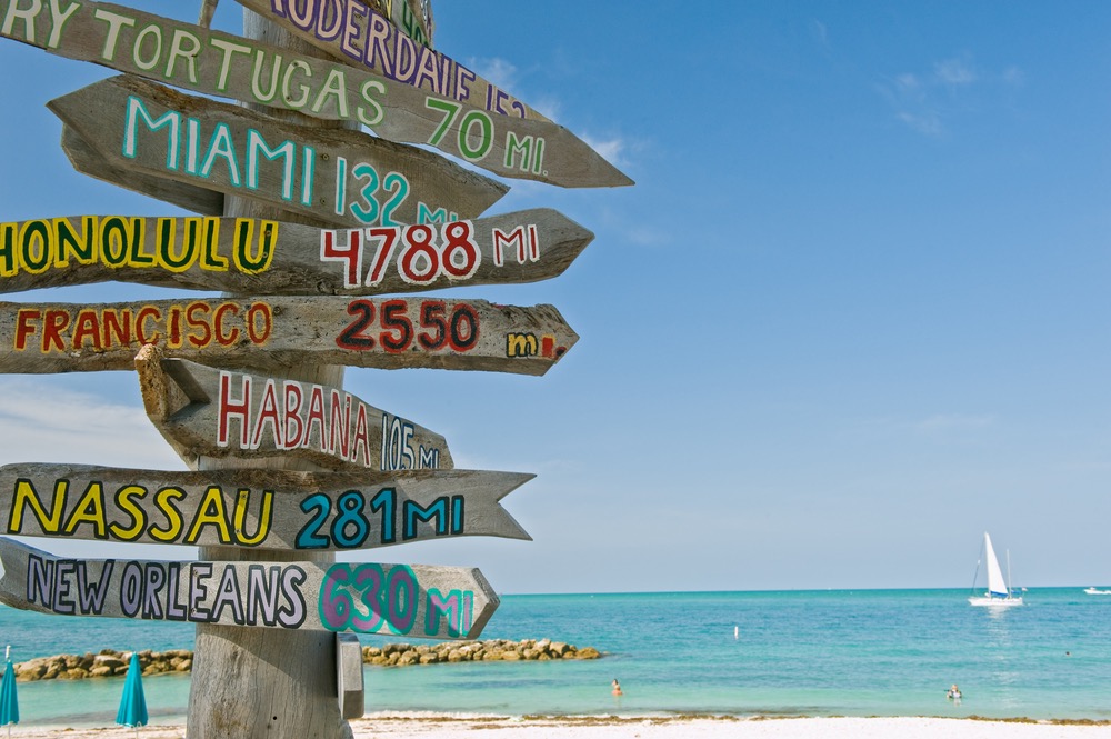 Florida Keys Online, key west at beach with wooden sign showing distances to various locations